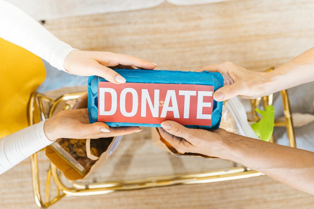 Donate Now Hands exchanging a donation box filled with items, symbolizing giving and community support.